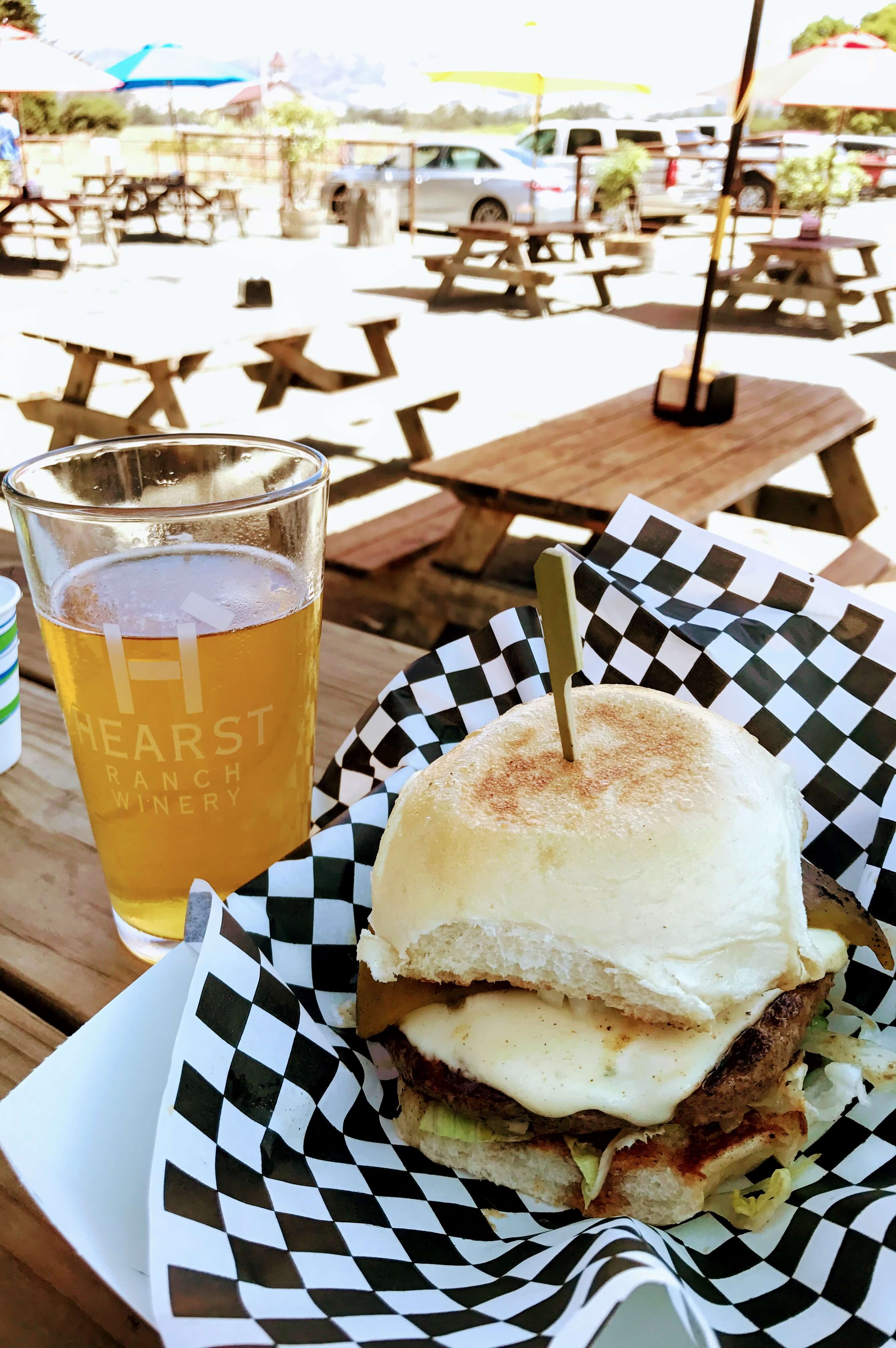 Juicy, cheesy, burger and beer on a picnic table in the sun