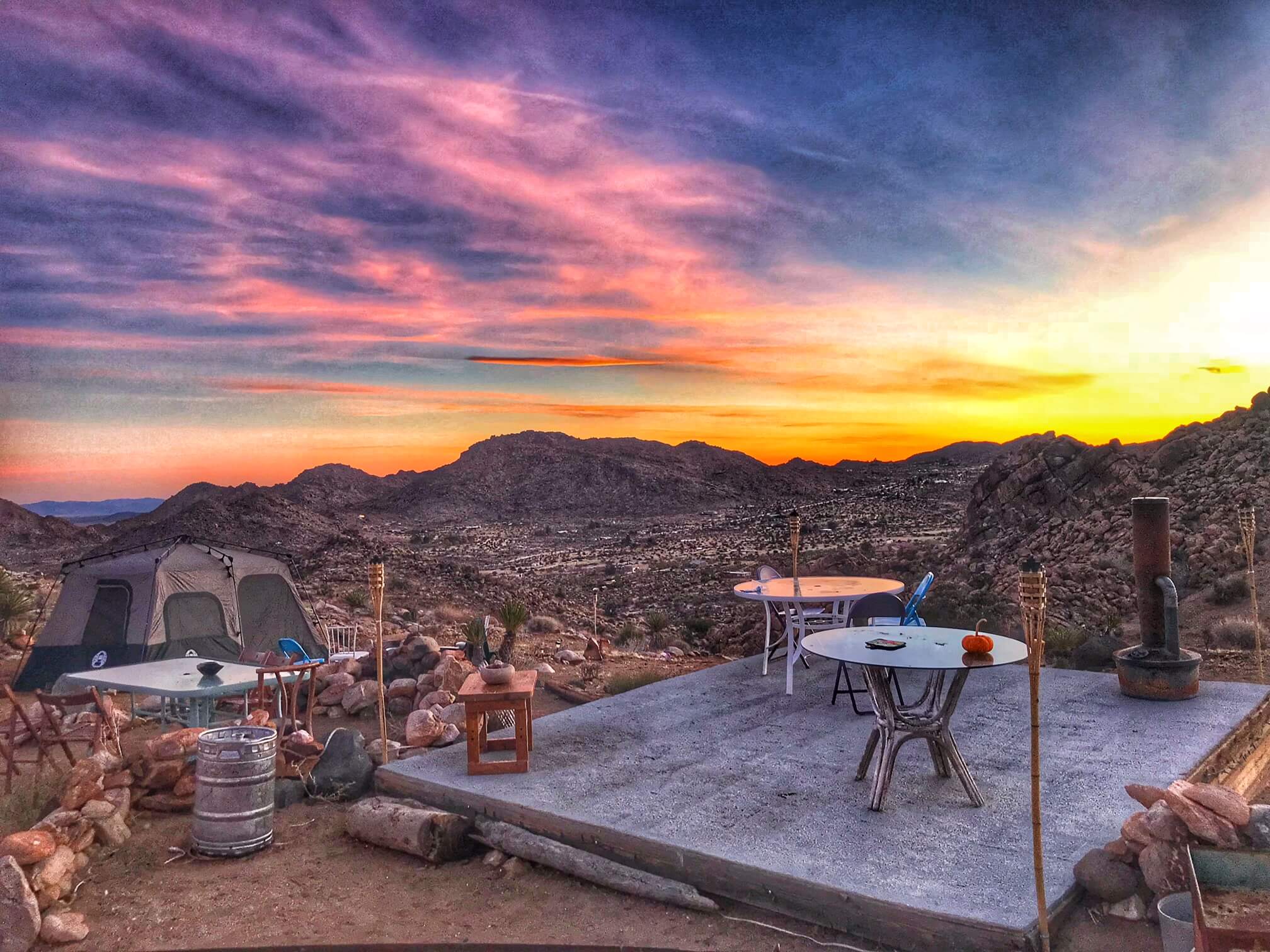 Gorgeous sunrise in yellow, pink, orange and blue over the joshua tree desert. There are table and a tent in the foreground.