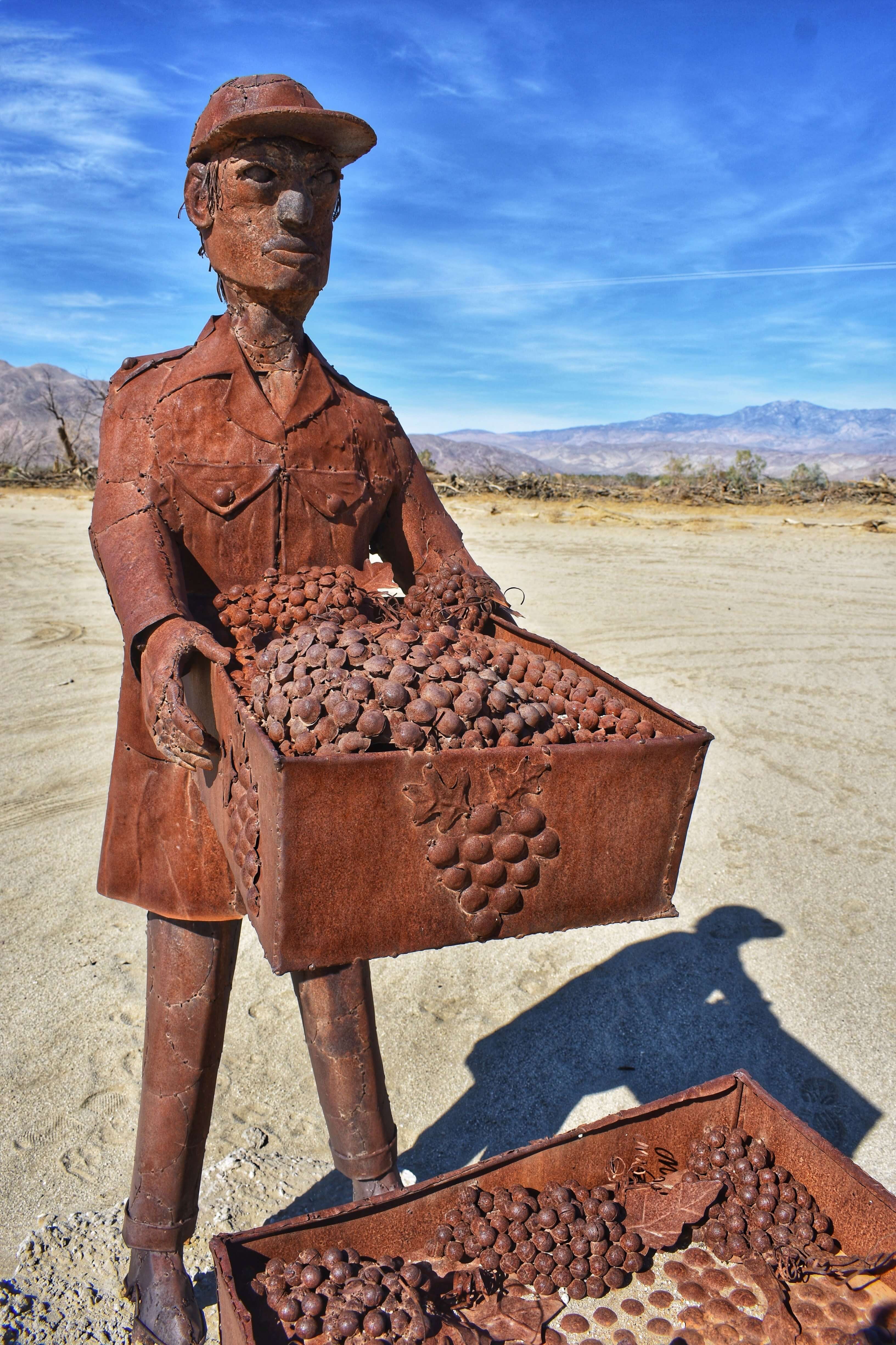 Sculpture of a man wearing a hat carrying a box full of grapes