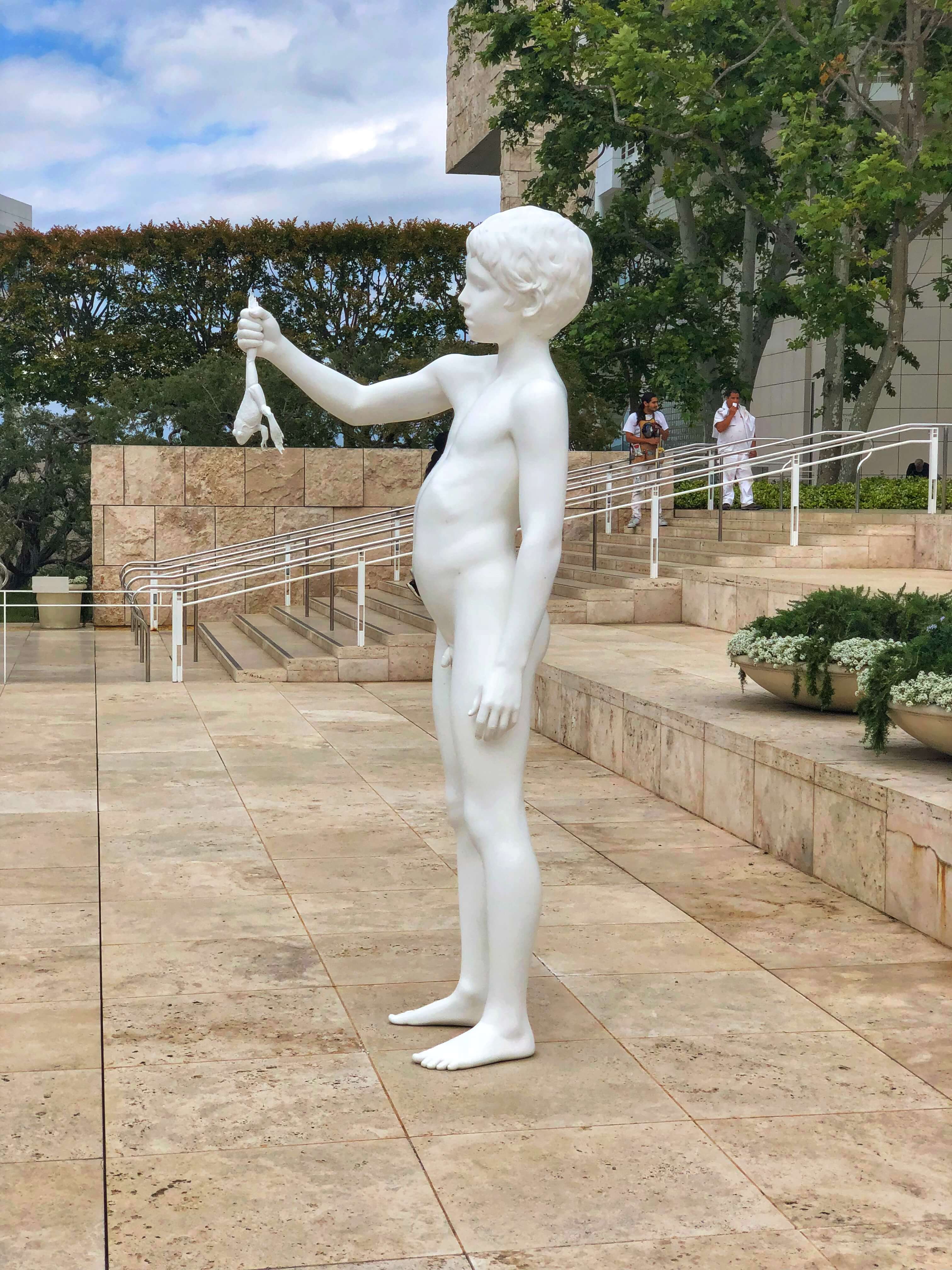 statue of a little boy holding up a frog by his hind leg outside of the getty museum 