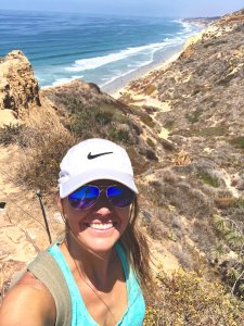 My friend Amy wearing a white hat hiking you can see cliffs and an ocean in the background