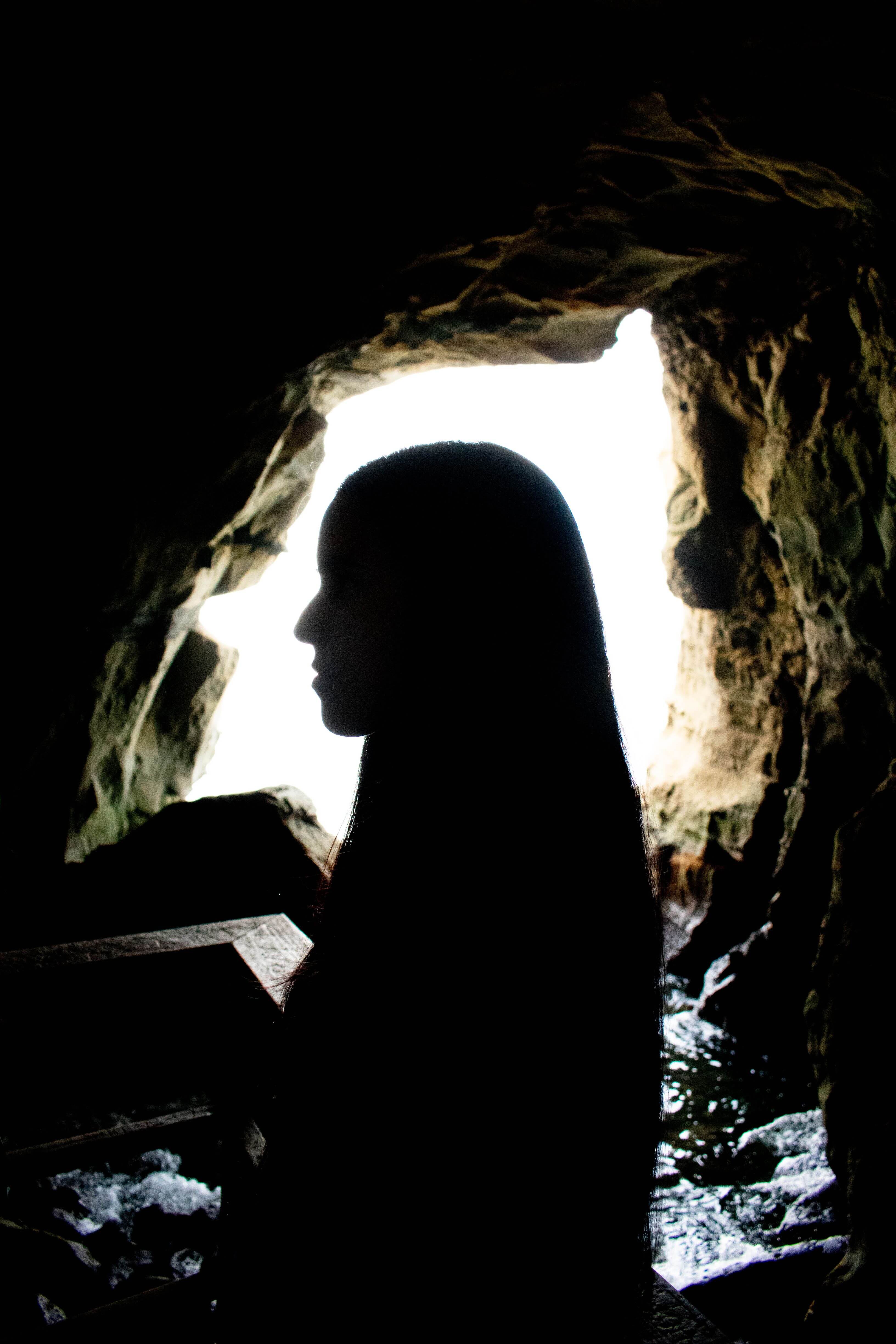 a girls profile trying to match the face formation in the rock inside a sea cave