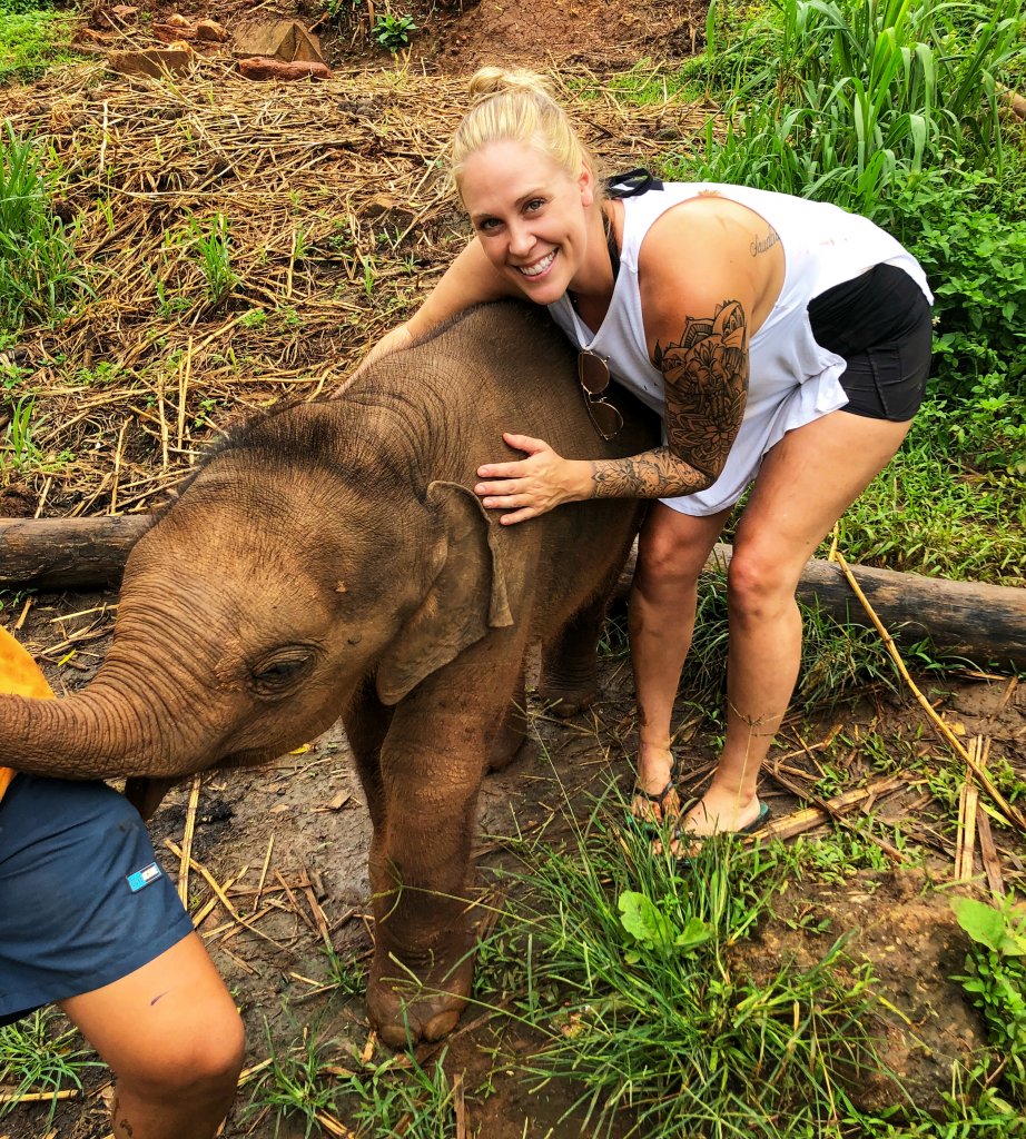 me bending down smiling next to a baby elephant